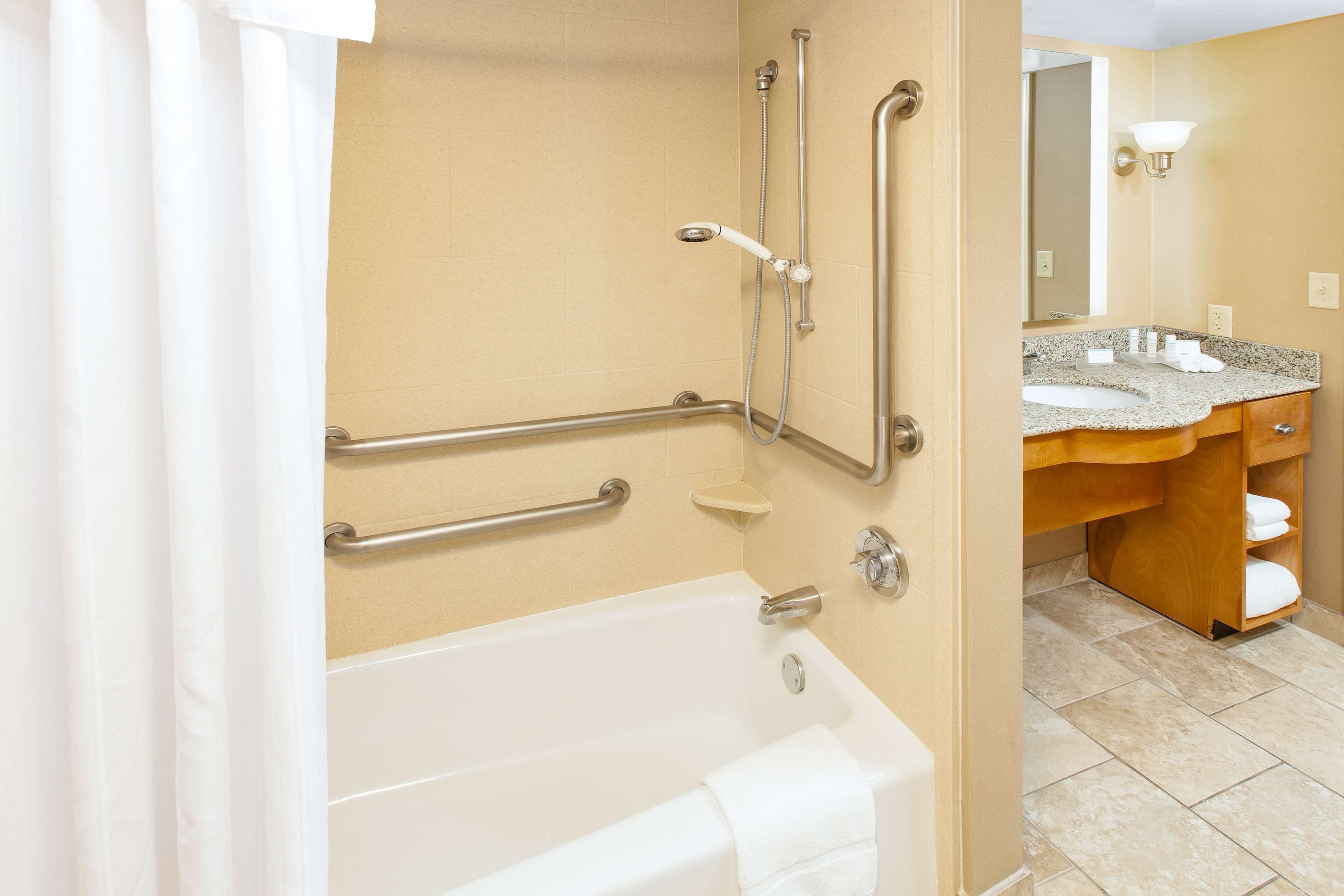 A bathroom with a bathtub, grab bars, a sink, and a mirror.