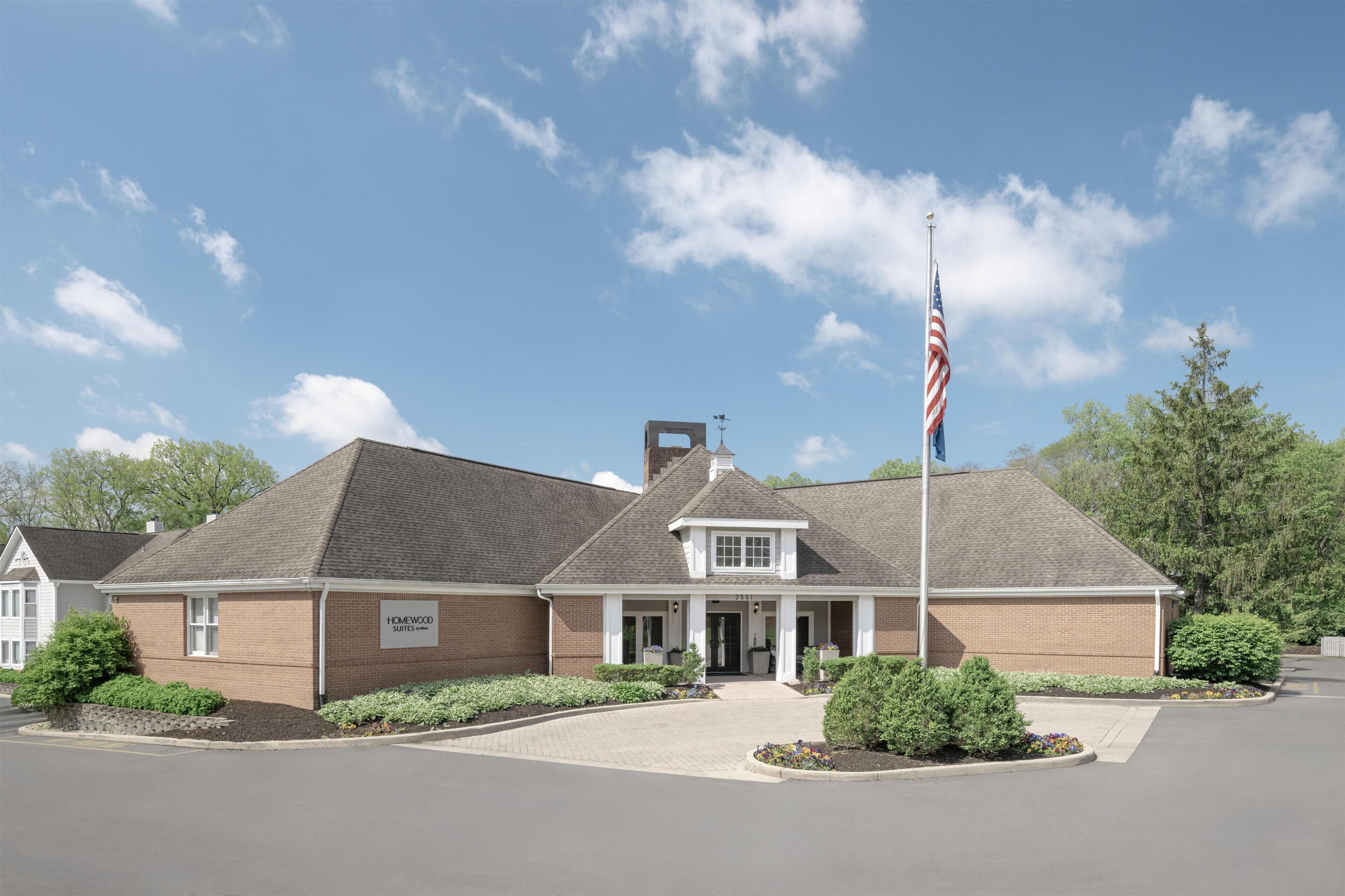A two-story building with a brick facade, a flagpole with an American flag, and a landscaped entrance area.