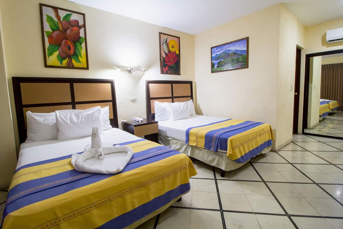 A hotel room with two beds, each with a striped bedspread, a nightstand, and a wall-mounted lamp.