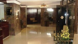A lobby with a reception desk, a seating area, and a reception desk with a flower arrangement. - Ambassador (Mérida)