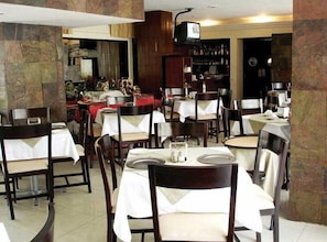 A restaurant with multiple tables and chairs, a television mounted on the wall, and a bar area in the background. - Ambassador (Mérida)