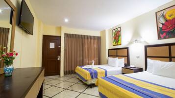 A hotel room with two beds, a TV, a desk, and a vase of flowers.