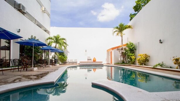 A swimming pool with lounge chairs and umbrellas, surrounded by white walls and greenery. - Ambassador (Mérida)