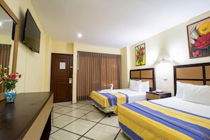 A hotel room with two beds, a TV, a desk, and a vase with flowers.