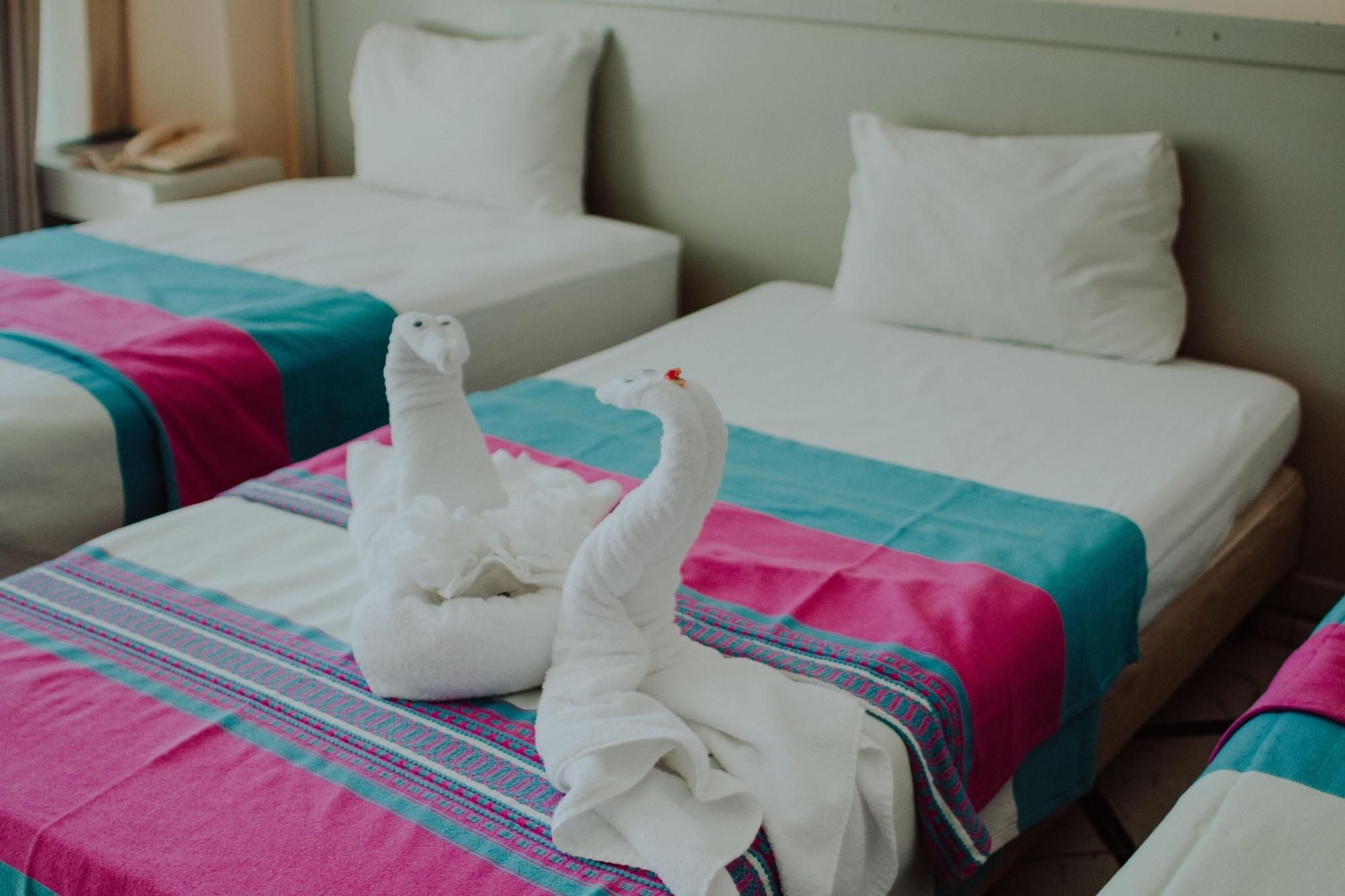 A hotel room with two beds, each with a white headboard and a colorful blanket.