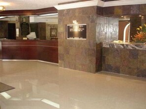 A reception area with a stone wall, a reception desk, and a plaque. - Ambassador (Mérida)