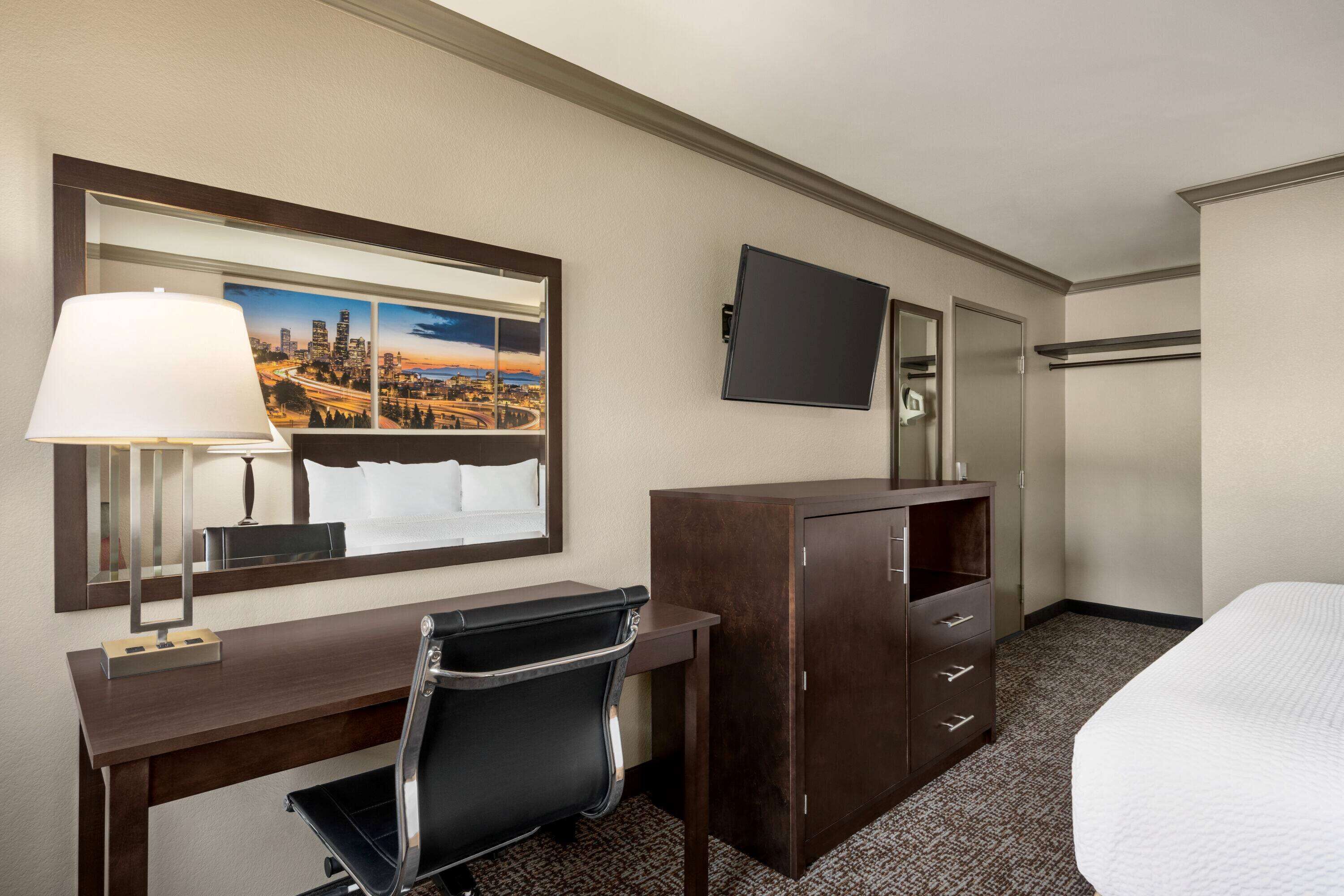 Une chambre d’hôtel comprenant un lit, un bureau avec une chaise, une commode, une télévision et un grand miroir.