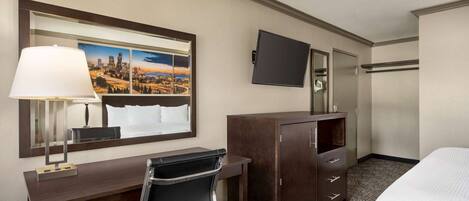 A hotel room with a bed, a desk with a chair, a dresser, a TV, and a large mirror.