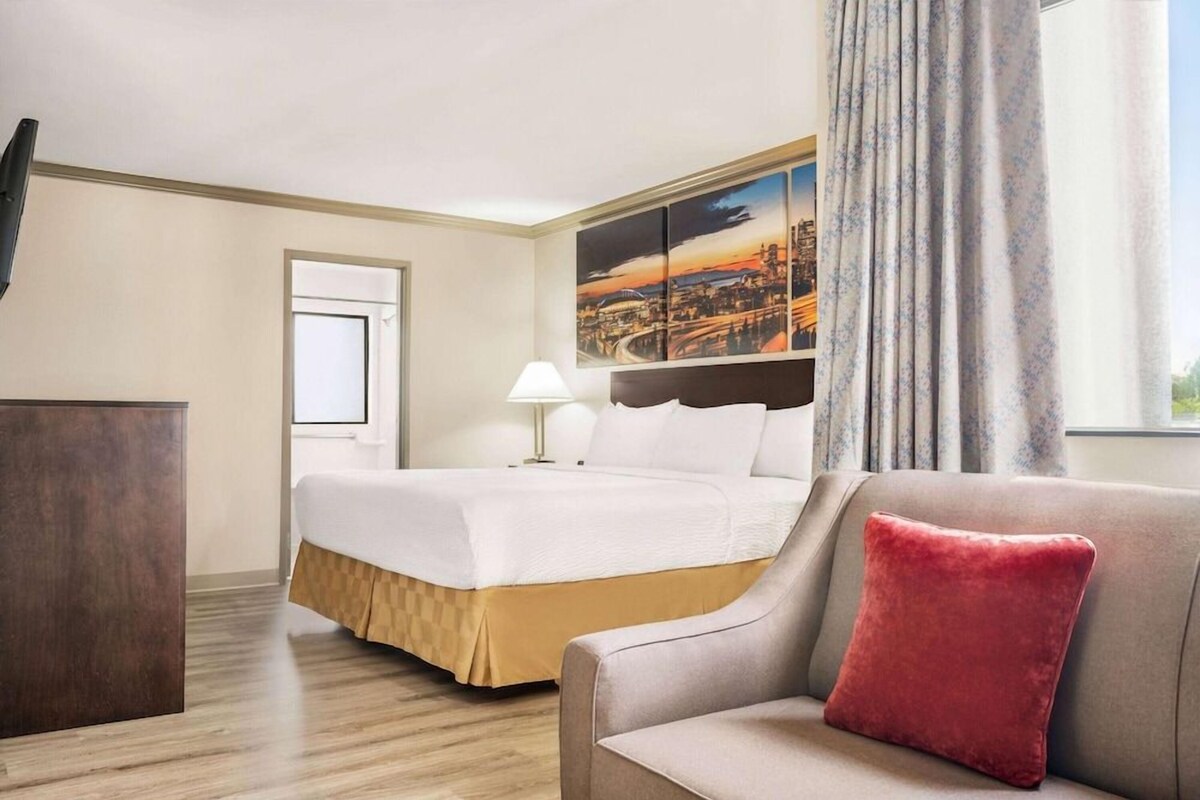 Habitación de hotel con cama, escritorio, lámpara, sofá y una pintura de paisaje urbano en la pared.