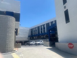 Un área de estacionamiento con una señal de parada, la entrada de un edificio y dos camiones estacionados.