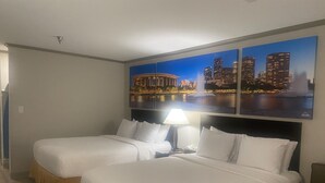 Habitación de hotel con dos camas, una mesita de noche con lámpara y un cuadro grande con una vista de la ciudad.