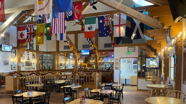 Interior de un restaurante con varias mesas y cabinas, vigas de madera y banderas colgando del techo.