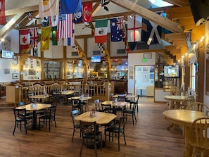 A restaurant interior with multiple dining tables and booths, wooden beams, and flags hanging from the ceiling. - Clarion Inn Near China Lake Naval Station (Ridgecrest)