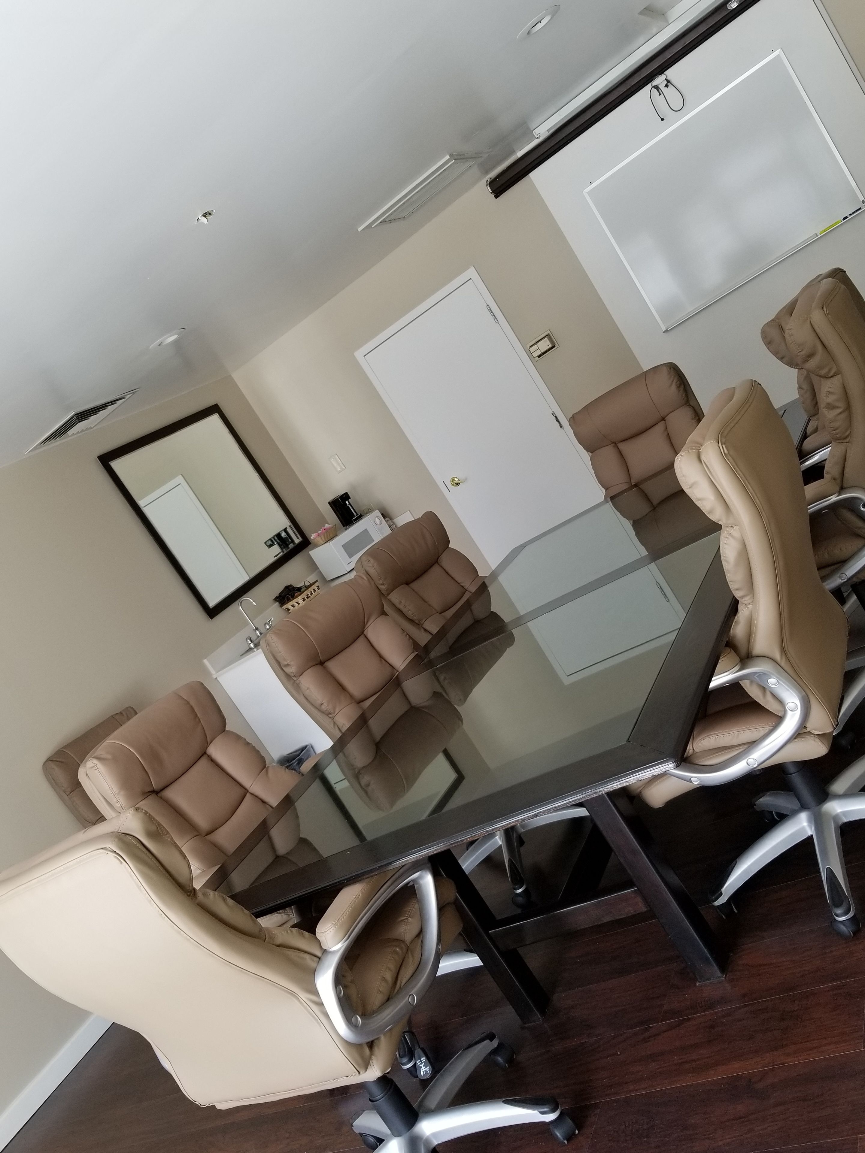 Un salón de conferencias con una mesa de vidrio, sillas de cuero color crema y una puerta blanca, además de una pizarra.