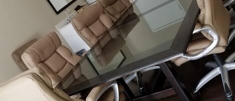Un salón de conferencias con una mesa de vidrio, sillas de cuero color crema y una puerta blanca, además de una pizarra.
