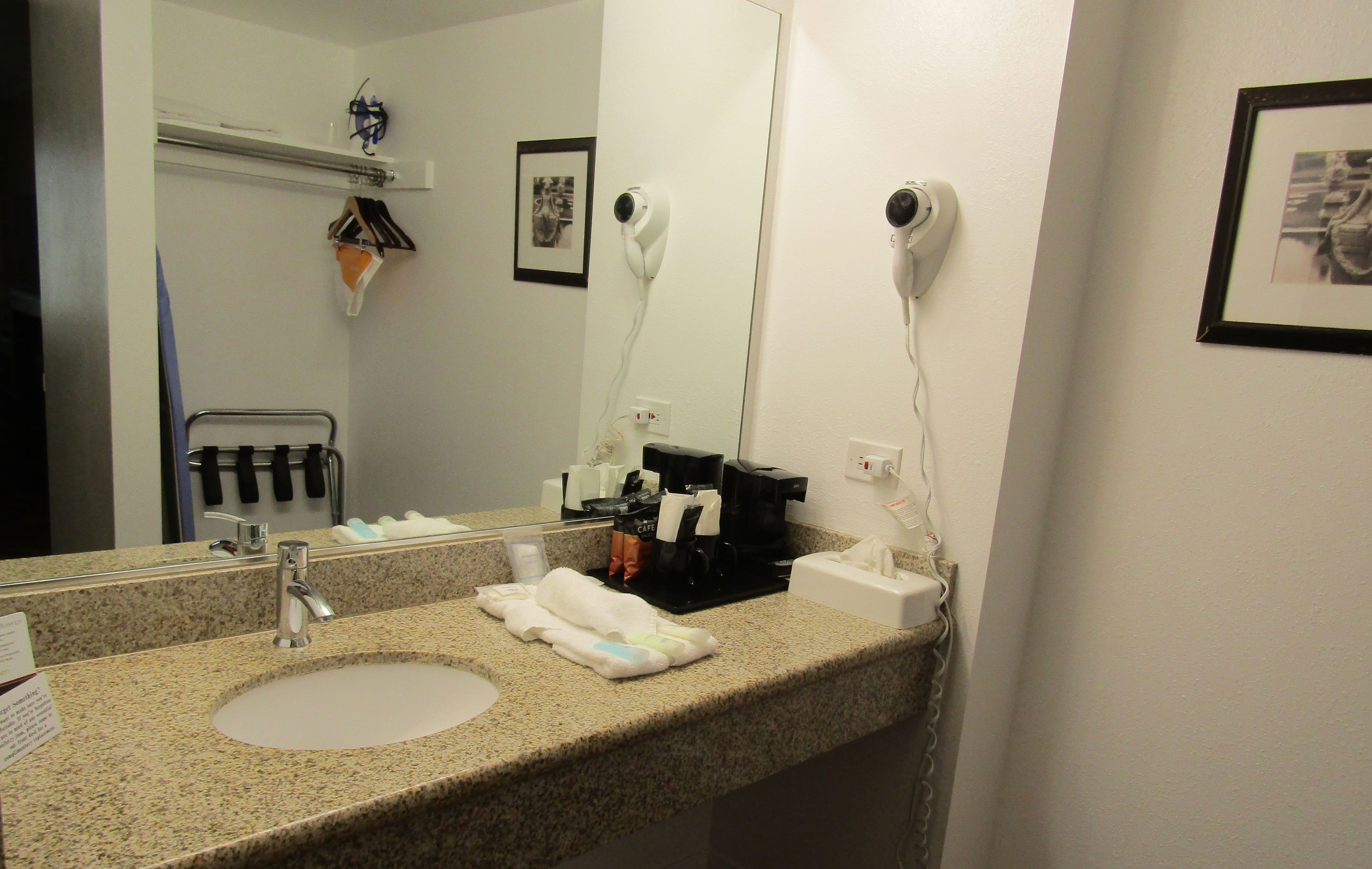 Un baño con encimera de granito, lavabo, espejo, secador de pelo y toallero.