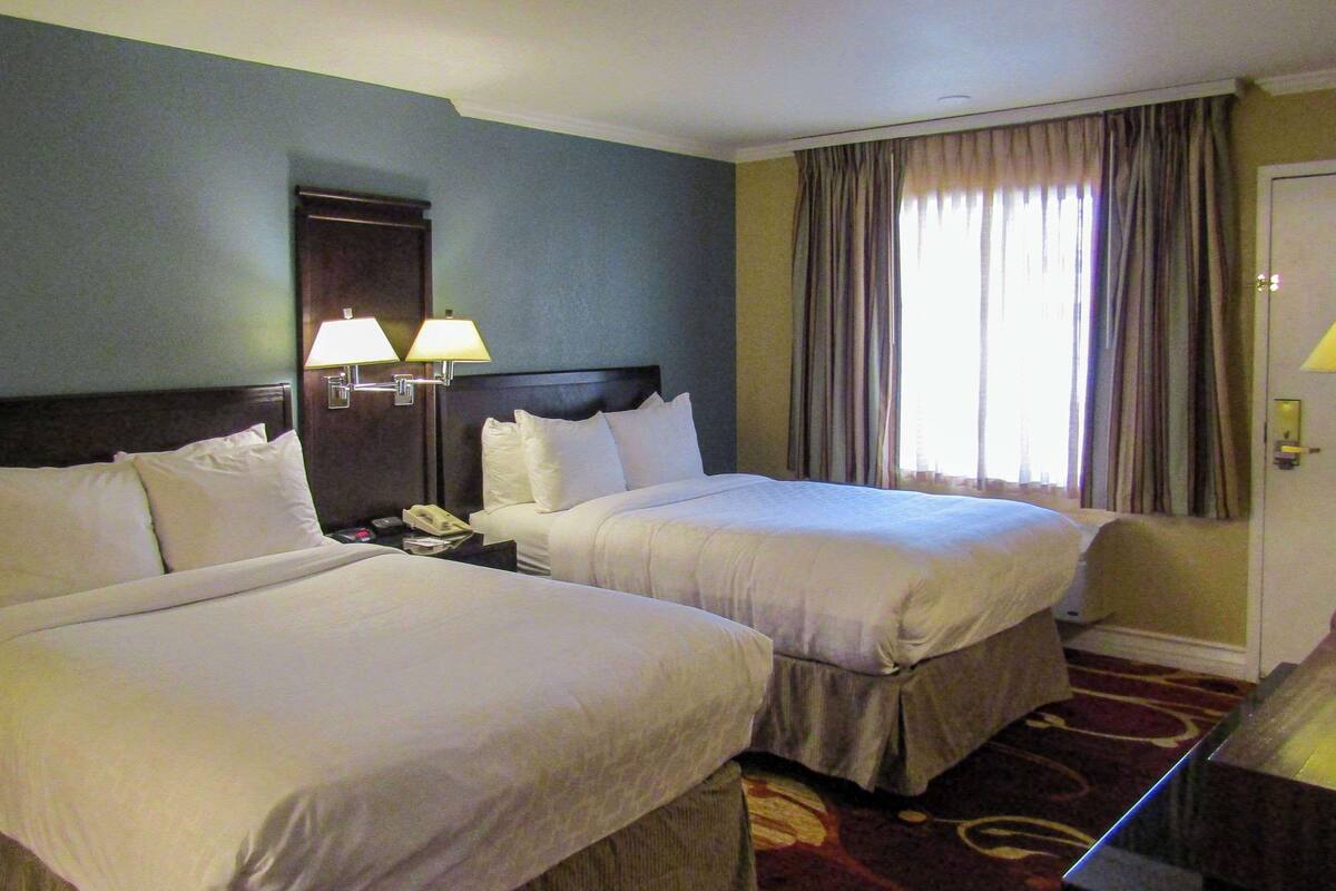 A hotel room with two beds, a nightstand with a lamp, a telephone, and a window with curtains.