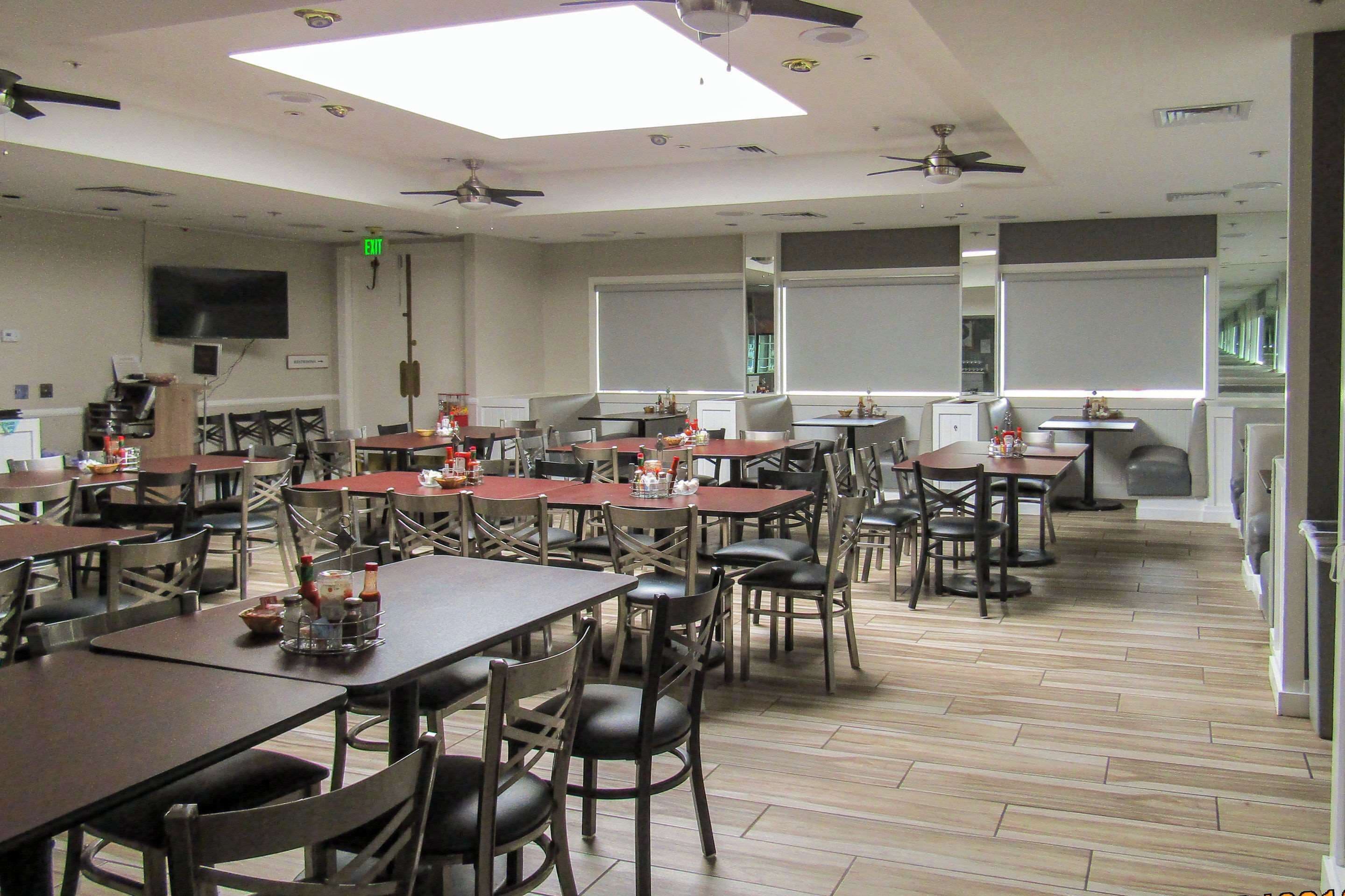 A spacious dining area with multiple tables and chairs, ceiling fans, and a large window providing natural light.