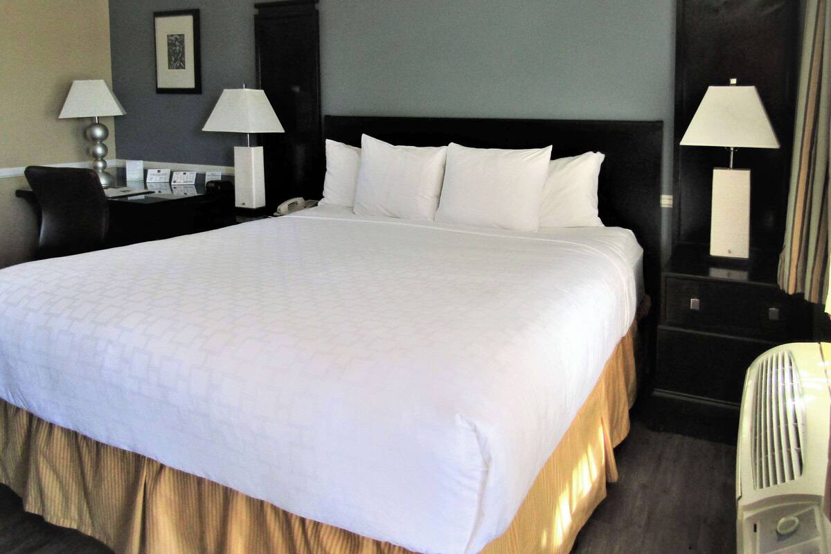 A hotel room with a large bed, two bedside tables with lamps, a desk with a chair, and a wall-mounted phone.