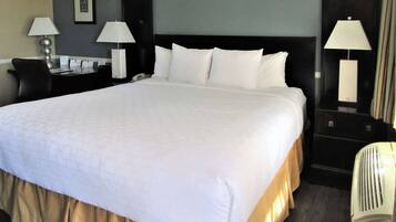 Una habitación de hotel con una cama grande, dos mesitas de noche con lámparas, un escritorio con silla y un teléfono en la pared.