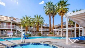 Un hotel con piscina, palmeras y una zona cubierta con sillones de descanso.