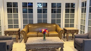 Una habitación con un sofá de cuero marrón, dos sillones a juego, una mesa de centro de mármol y un jarrón con flores.