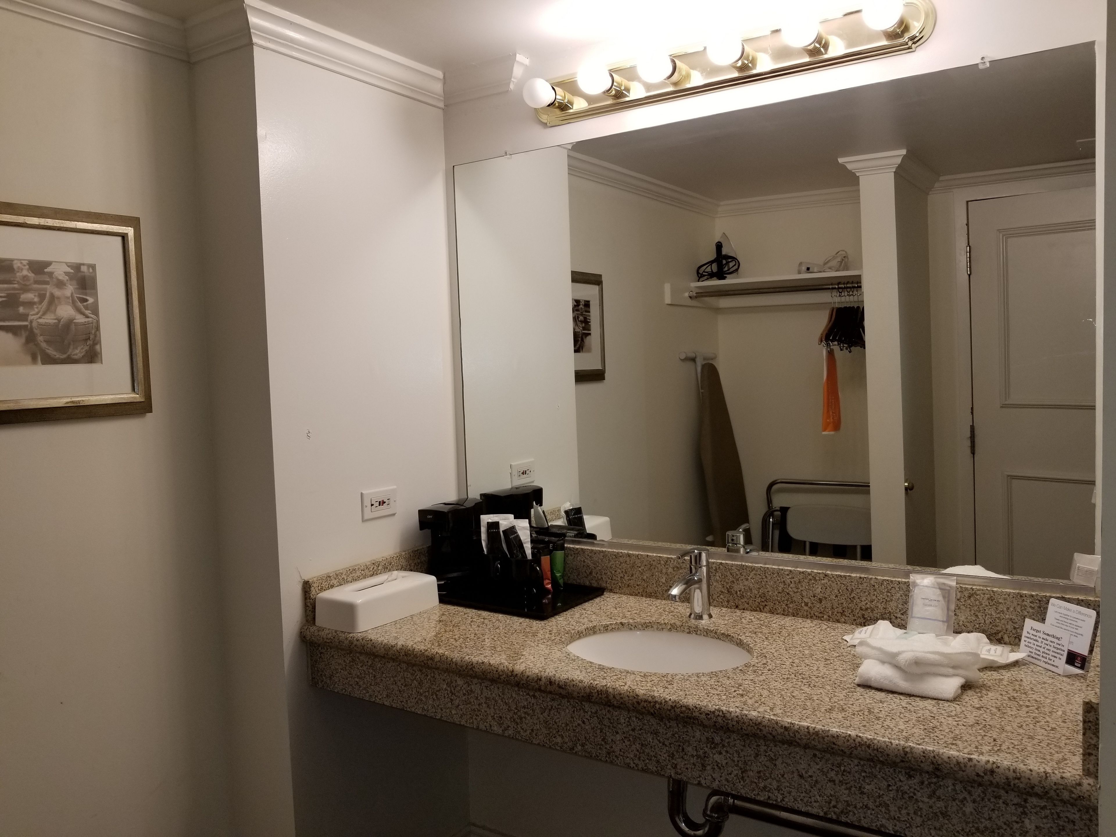 Ein Badezimmer mit Granitplatte, Waschbecken, einem beleuchteten Spiegel, einem Handtuchhalter und einem gerahmten Bild an der Wand.