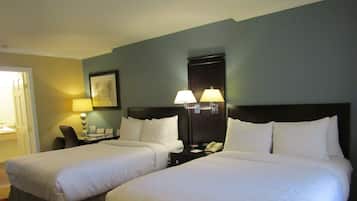 A hotel room with two beds, a nightstand with a lamp, a framed picture on the wall, and a door to the left.