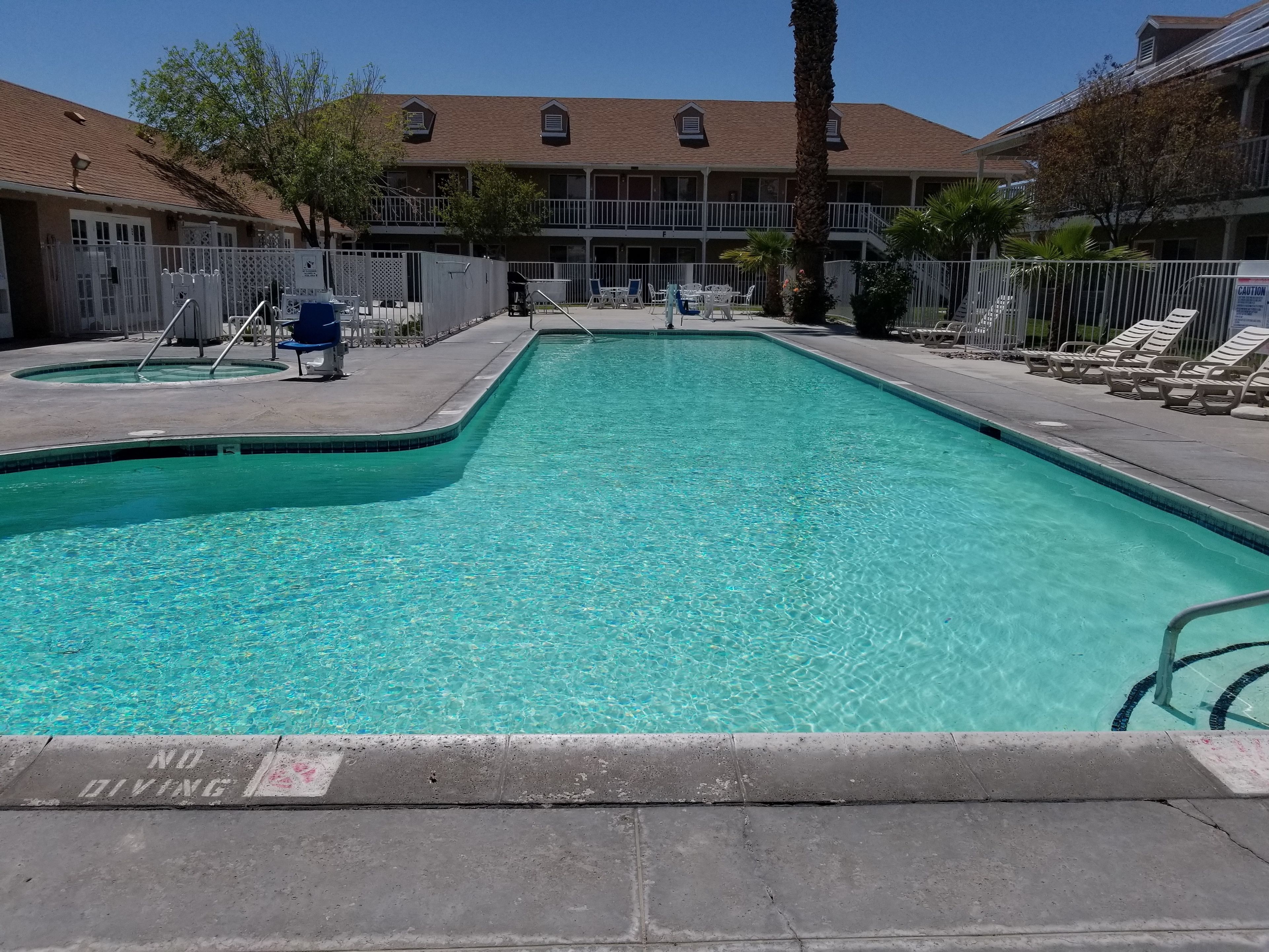 A rectangular swimming pool with a no diving sign, surrounded by lounge chairs and a building with a tiled roof.