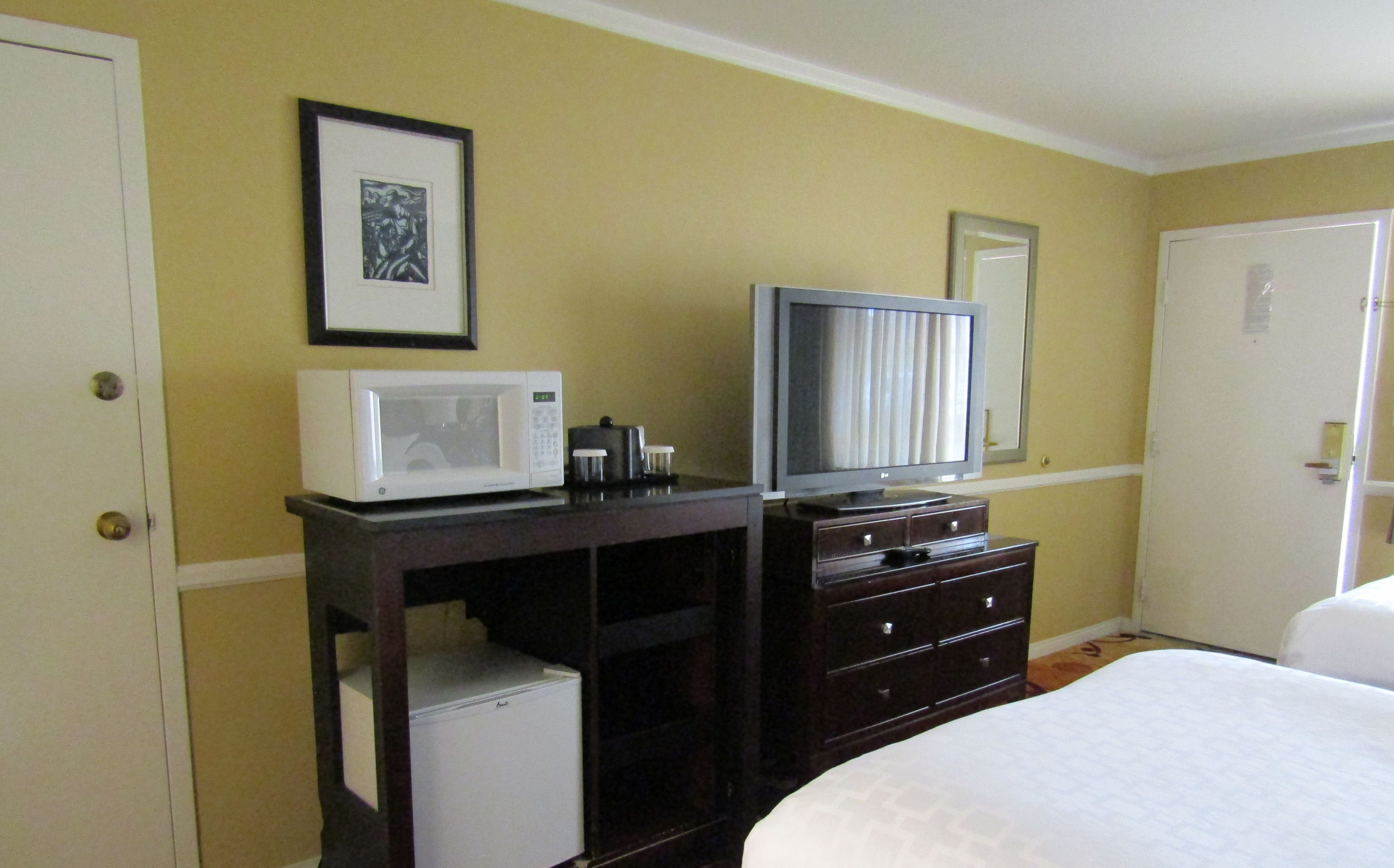 A hotel room with a bed, a dresser, a microwave, a television, and a refrigerator.