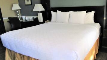 A large bed with a white comforter and a gold skirt, a nightstand with a lamp, and a framed picture on the wall.