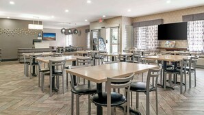 A spacious dining area with multiple tables and chairs, a reception desk, and a large flat-screen TV mounted on the wall. - Best Western Beacon Inn (Grand Haven)