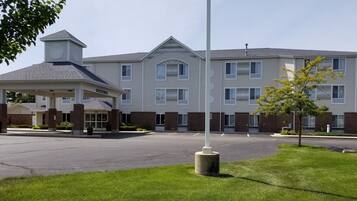 A multi-story hotel with a covered entrance, a parking lot, and a well-maintained lawn.