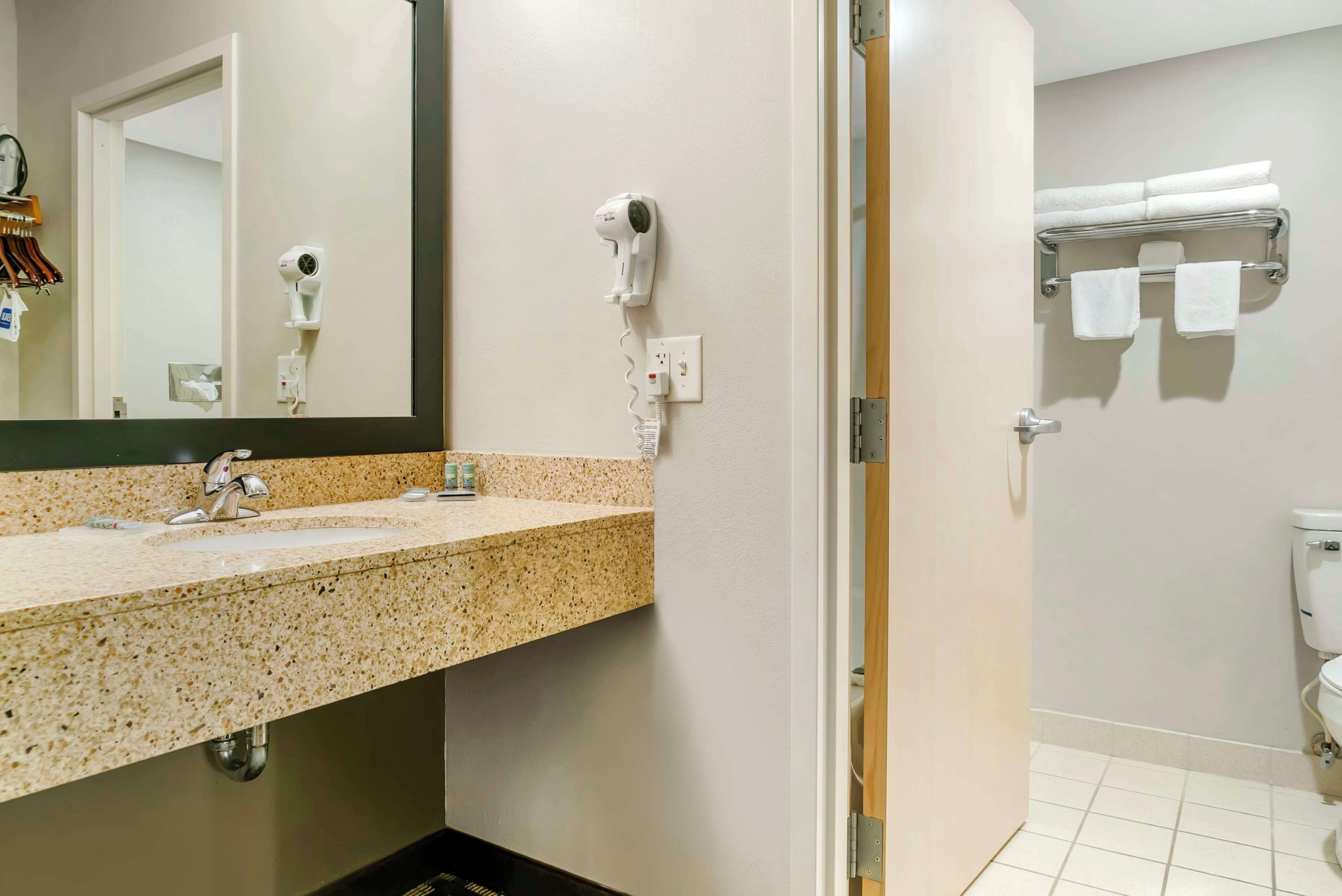 A bathroom with a granite countertop sink, a hairdryer, and a towel rack with towels.