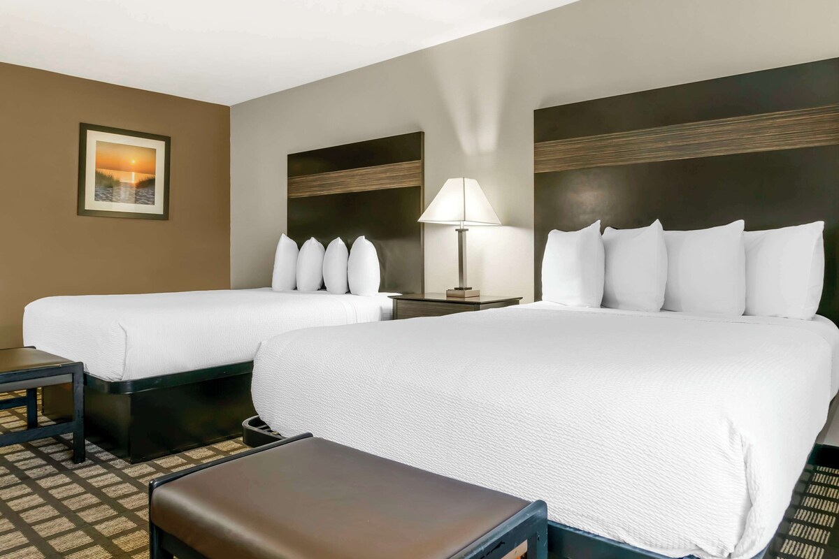 A hotel room with two beds, a nightstand, a lamp, and a picture on the wall.