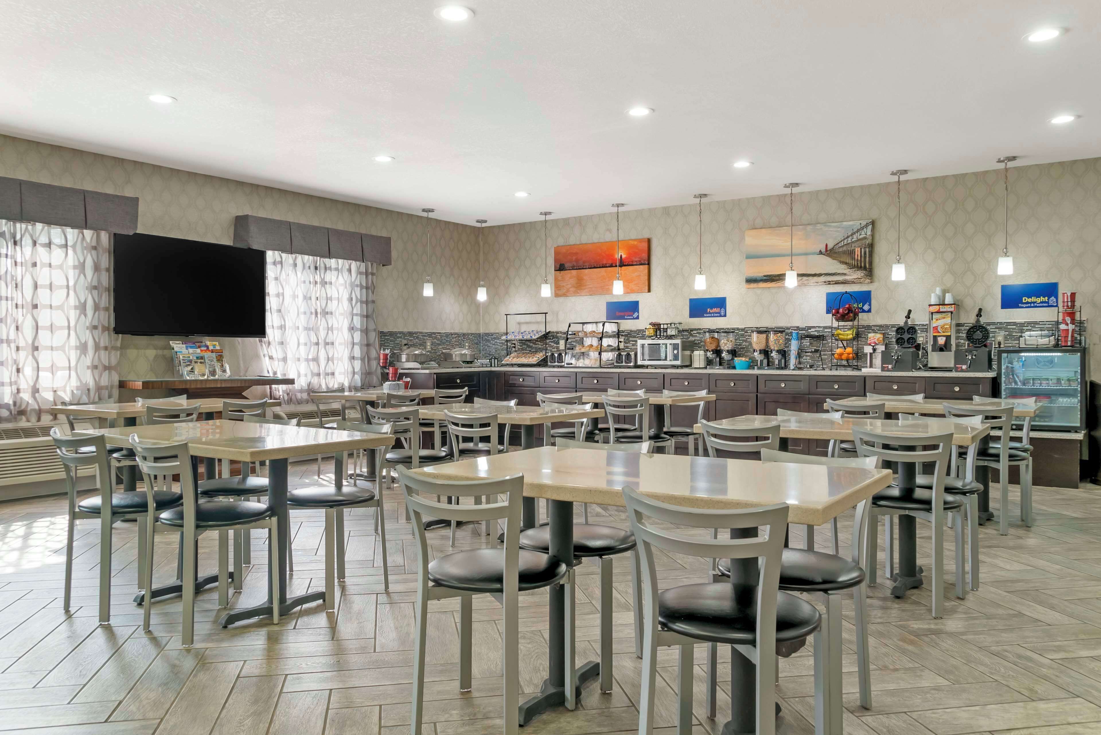 A spacious restaurant with multiple tables and chairs, a kitchen area, and a flat-screen TV mounted on the wall.