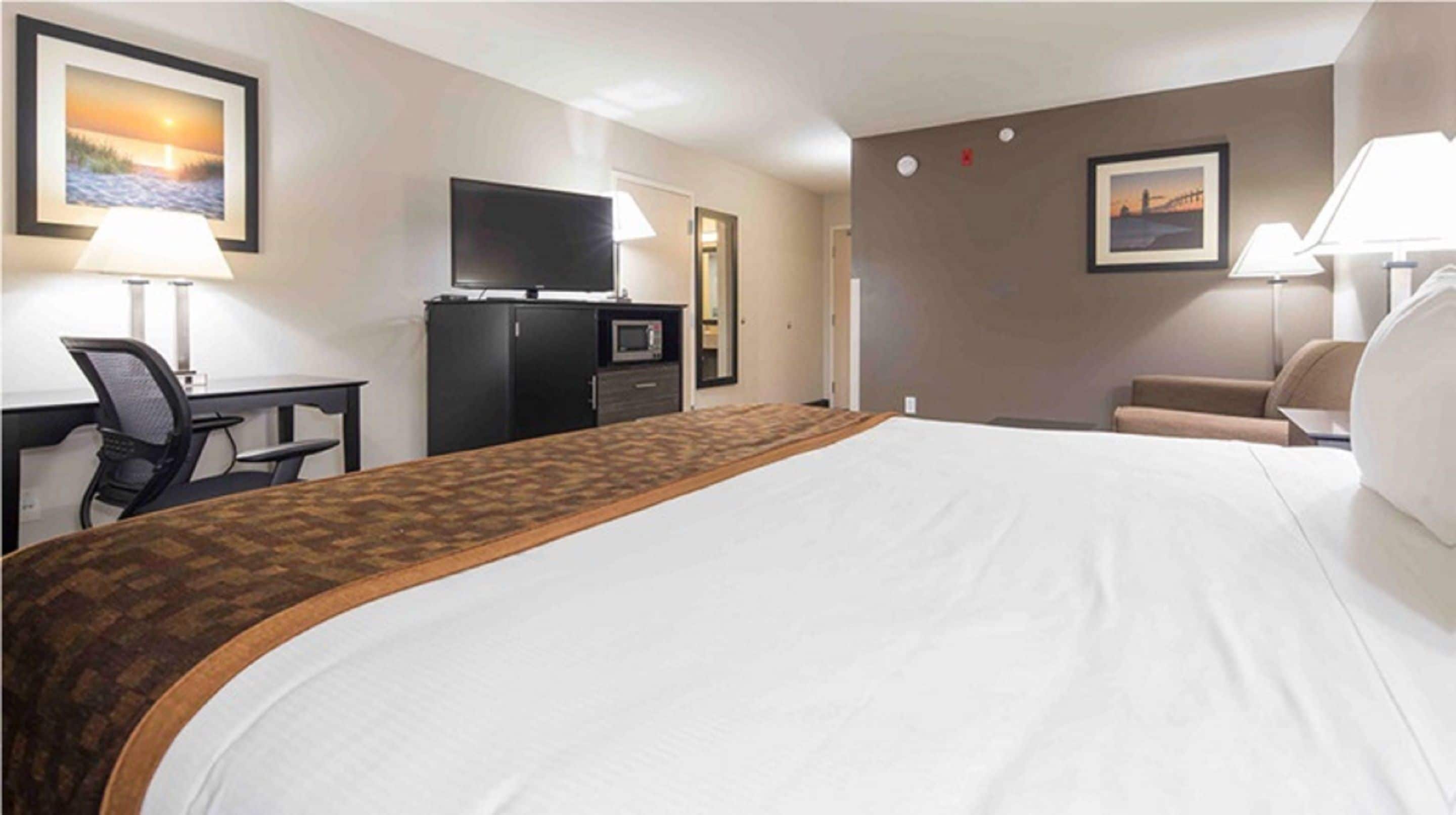Une chambre d’hôtel avec un grand lit, un bureau avec une chaise, une télévision et deux lampes.