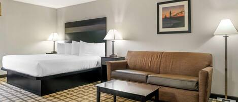 A hotel room with a bed, a sofa, a coffee table, and two lamps.
