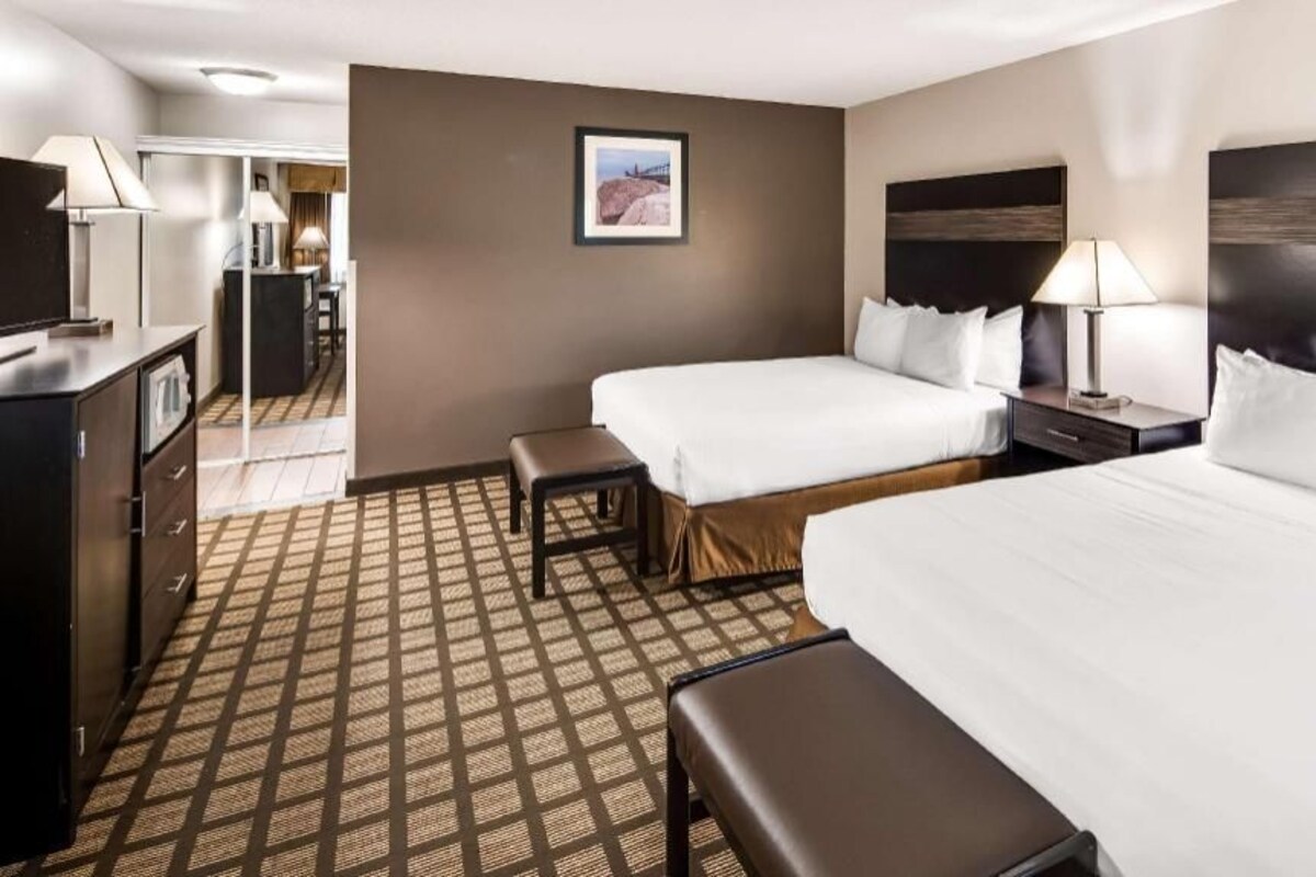 A hotel room with a large bed, two smaller beds, a desk, a chair, a TV, and a picture on the wall.