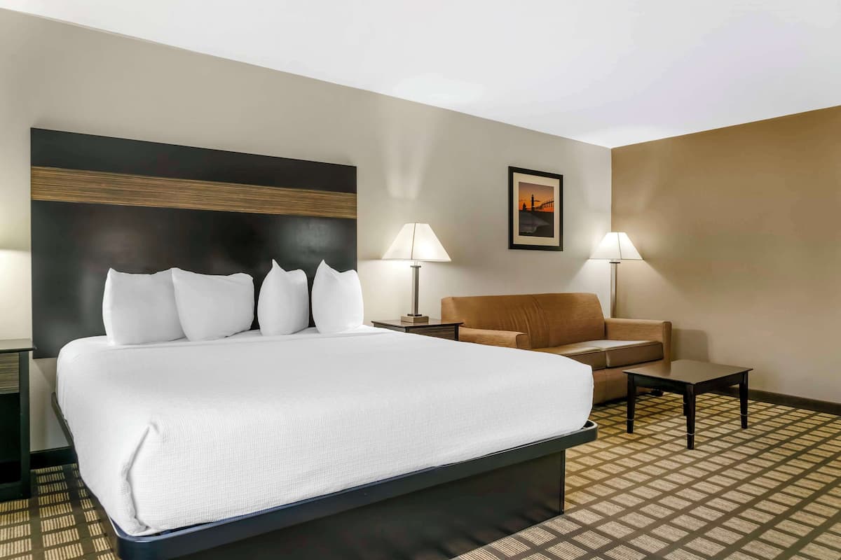 A hotel room with a large bed, a brown sofa, two side tables with lamps, and a patterned floor.