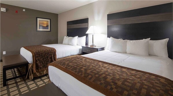 A hotel room with two beds, a desk, a lamp, and a picture on the wall.