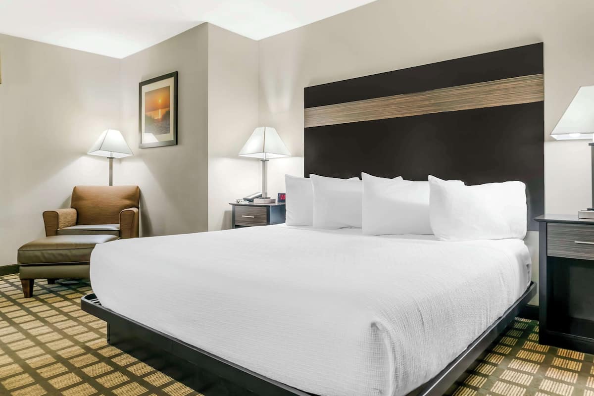A hotel room with a large bed, a chair, two bedside tables, and a wall-mounted lamp.