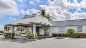A hotel entrance with a covered parking area, a palm tree, and a building with a grey roof. - Quality Inn Downtown Stuart (Stuart)