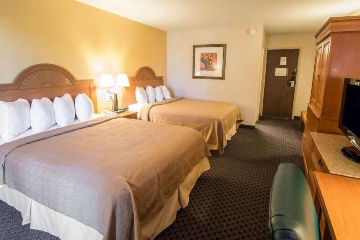A hotel room with two beds, a desk, a chair, a television, and a framed picture on the wall.