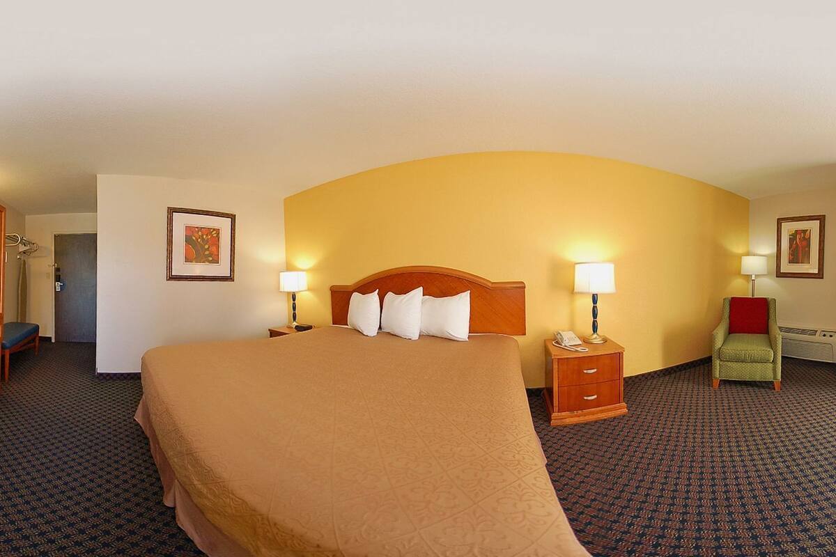 A hotel room with a large bed, two bedside tables with lamps, a chair, a desk, and a wardrobe.