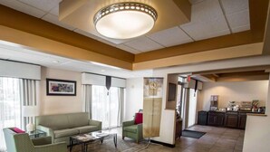 A hotel lobby with a sofa, armchairs, a coffee station, and a view of the kitchen. - Quality Inn Downtown Stuart (Stuart)