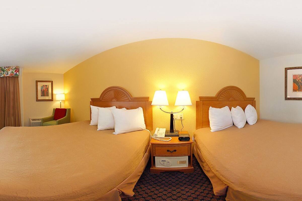 A hotel room with two beds, a nightstand with a lamp, a telephone, and a chair.