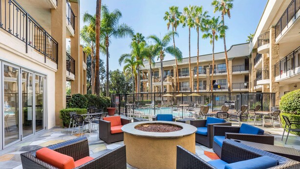 An outdoor seating area with wicker furniture, a central fire pit, and a pool in the background. - Comfort Inn & Suites Orange County John Wayne Airport (Santa Ana)