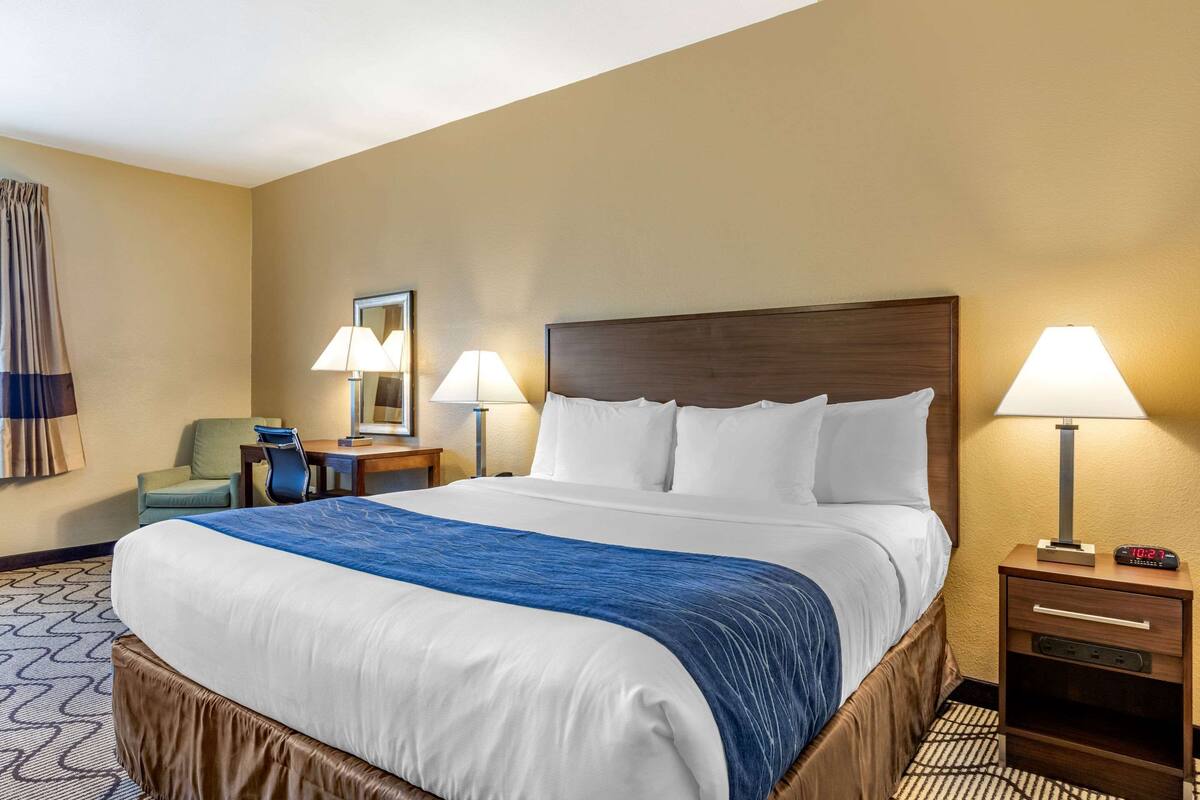 Una camera d'albergo con un letto grande, due comodini con lampade, una sedia e una scrivania.