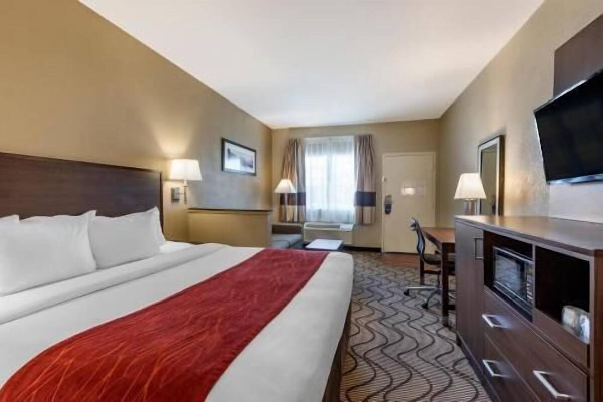 Una camera d'albergo con un letto grande, una scrivania, una televisione e una finestra con tende.